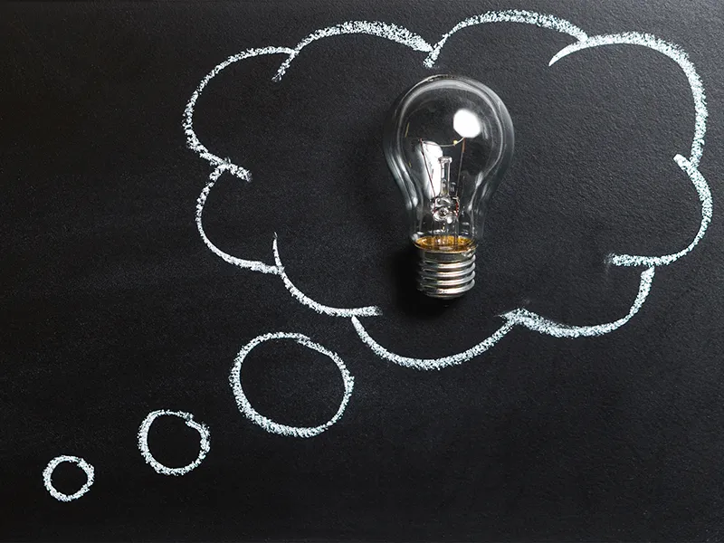Thought bubble drawn on chalkboard, with real lightbulb inside the bubble.