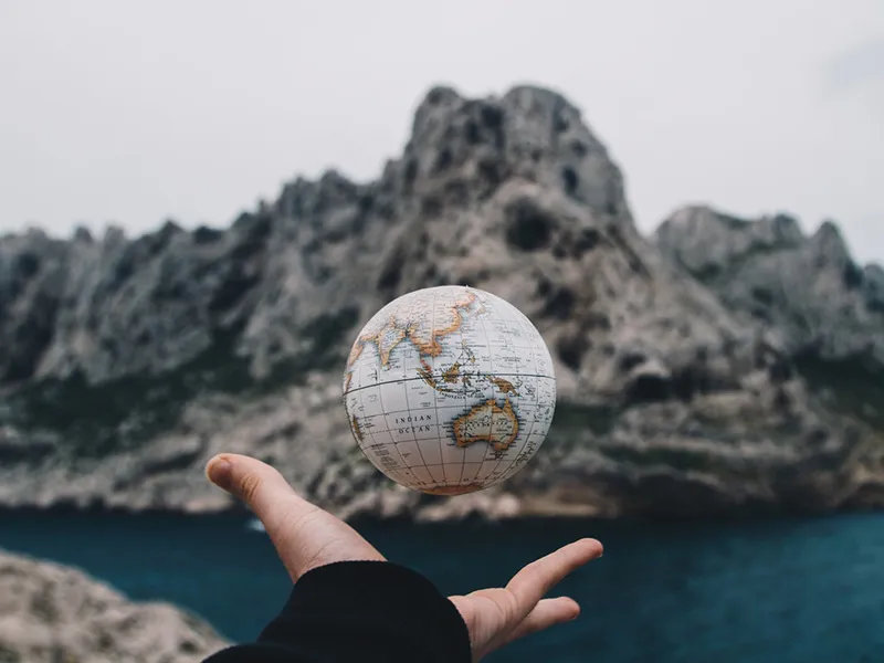 A hand holds a floating globe above it, with a serene ocean in the background.