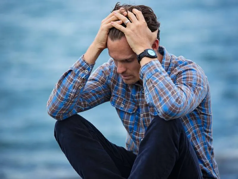A stressed man sits with his hands in his hair, conveying a sense of frustration and overwhelm.